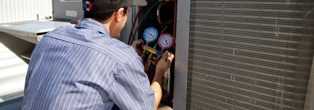 HVAC technician servicing a condenser unit in Watertown